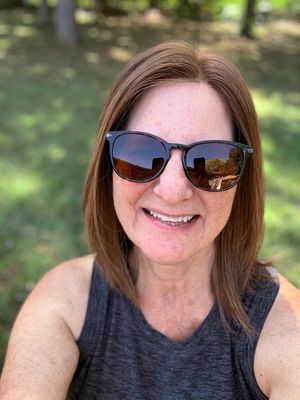 Woman_with_brown_hair_wearing_sunglasses_and_a_gray_tank_top_smiling.jpg